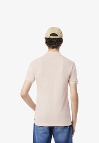 Ljusrosa polo t-shirt med korta ärmar, har en krage och en enkel design, tillsammans med blå jeans. En beige baseballkeps bärs.