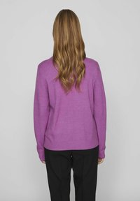 Lila stickad tröja med långa ärmar, ribbade muddar och fåll. Bärs med svarta byxor som har en slät yta och avslappnad passform.