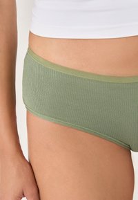 Zielone bokserki z prążkowanej tkaniny, z gładką talią, o gładkiej fakturze i dopasowanym kroju, częściowo pokazane na skórze.