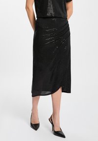 Gonna midi nera realizzata in tessuto testurizzato con un sottile motivo di paillettes, davanti drappeggiato e orlo inclinato, abbinata a tacchi neri.