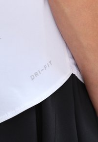Maglietta bianca DRI-FIT a maniche corte, con una texture liscia e un orlo. Il tessuto è leggero e traspirante, adatto per lo sport.