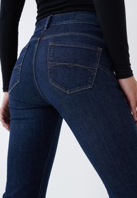Jeans ajustados de un azul oscuro, confeccionados en denim, con una cintura alta, bolsillos traseros con costura curvada y una textura suave.