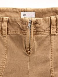 Beige denimbukser med høy midje, med metallglidelås og kroklukking, belte-løkker, og en etikett "GAP SANDY LIANG" inni.