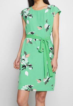 Vestido verde hasta la rodilla con estampados florales en blanco, negro y rosa, mangas tipo capa y un cinturón a juego atado en la cintura.