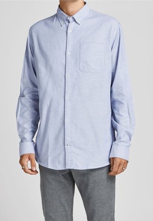 Camisa de manga larga azul claro con cuello con botones, bolsillo en el pecho y una textura sutil. Presenta botones blancos en la parte delantera.