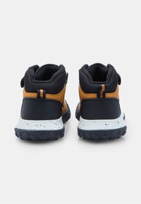 Un paio di sneakers per bambini nere e marroni con suole macchiate di bianco, mostrate da dietro su uno sfondo bianco.