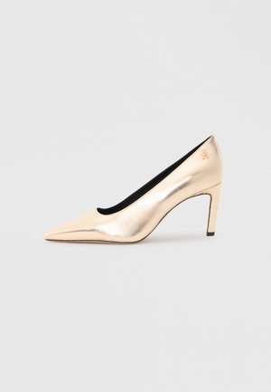 Beige metallic high-heeled pump with a pointed toe, smooth texture, and a black interior. Features a small logo detail on the heel.