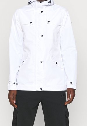 Person wearing a white hooded jacket with black snap buttons and black pants with cargo pockets standing against a plain background.