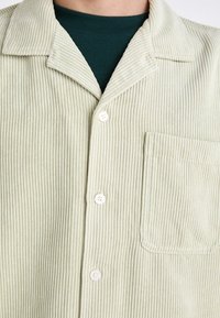 Lichtgroen corduroy shirt met een gestructureerd ribbelpatroon, puntige kraag en één borstzak. Voorzien van witte knopen en een gladde onderlaag.