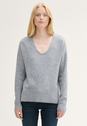 Grå strikket sweater med V-udskæring, ribbede manchetter og kant. Blød tekstur og en afslappet pasform, parret med mørke jeans.