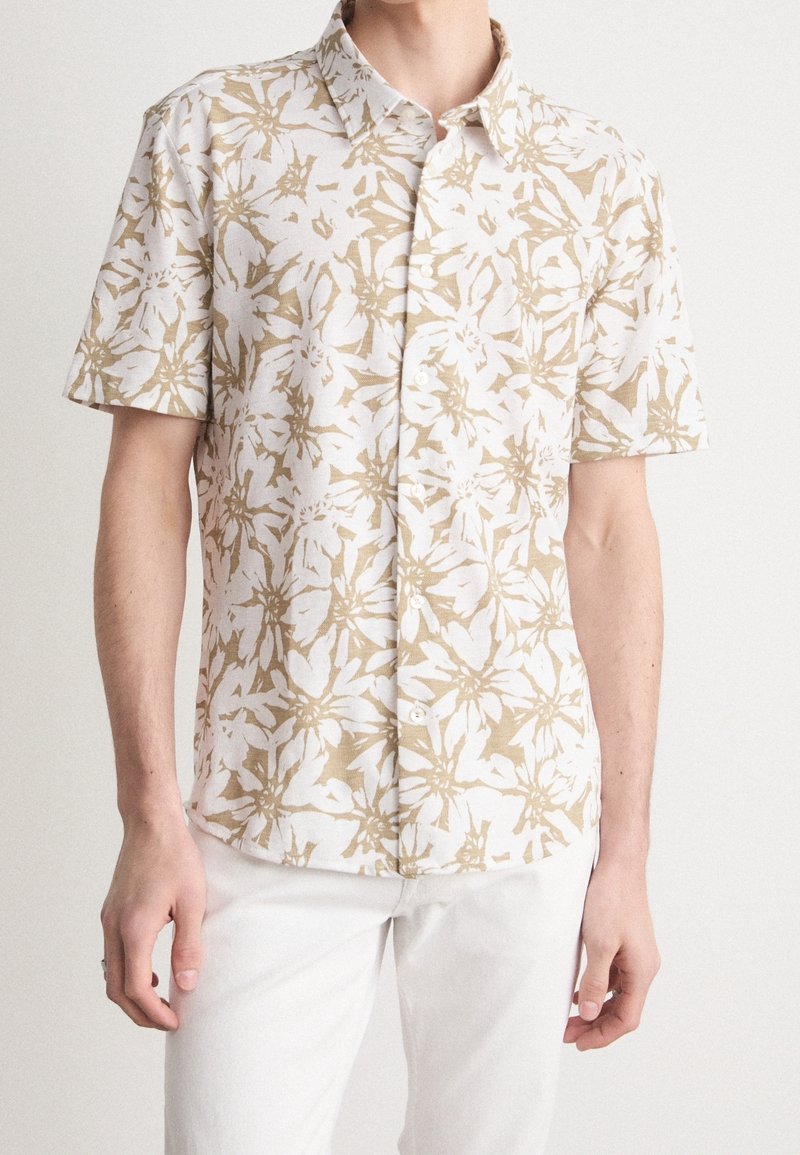 Camisetta a maniche corte realizzata in tessuto leggero, con un motivo floreale beige e bianco, chiusura con bottoni e colletto classico.