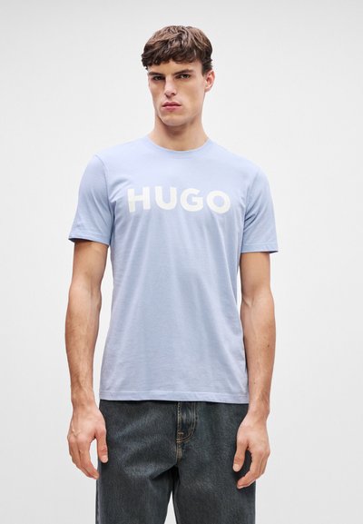 Светлосиня памучна тениска с къс ръкав, с думата "HUGO" написана с големи бели букви на гърдите. Прост дизайн с кръгло деколте.