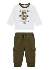 Chemise blanche à manches longues avec un motif imprimé vert et bleu marine, associée à un pantalon cargo vert olive avec des poches latérales et une taille élastique.