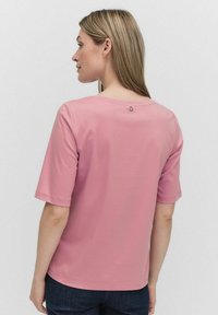 Rosa t-shirt med kort ärm och rund halsringning, med en liten rund accentknapp på baksidan, mjukt material och en avslappnad passform.