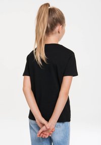 Black short-sleeve t-shirt made of cotton, featuring a round neckline. The model wears light blue denim jeans, seen from the back.