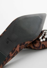 High Heel Schuh mit Leopardenmuster, das mit einem glatten, strukturierten Obermaterial und einer gemusterten Gummisohle versehen ist, geschmückt mit einem Strassakzent.