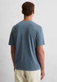 T-shirt à manches courtes, coupe décontractée, en coton bleu délavé. Doté d'un col rond et de détails de couture simples. La vue arrière montre une texture lisse.