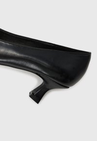 Zapato de tacón negro de cuero con punta redonda y un pequeño tacón cuadrado. Superficie lisa sin patrones visibles ni herrajes.