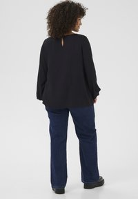 Black long-sleeve blouse with a keyhole back detail, paired with blue denim jeans. The textures are smooth and fitted, with flared legs.