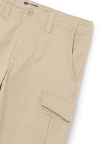 Pantalons cargo beiges en coton avec fermeture à bouton, dotés de poches latérales et d'une texture lisse et durable.