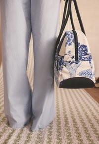 Tygpåse med blommönster i blått och vitt med svart botten. Har dubbla svarta handtag och en dragkedja upptill.