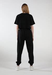 Schwarzes Baumwoll-Crop-Top und passende Jogginghosen mit elastischen Bündchen. Sichtbare weiße Sneakers. Glatte Textur, lässige Passform, minimales Design.