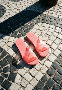 Sandales Havaianas rose corail posées sur un pavement en pavés noirs et blancs à motifs, avec une ombre proche.