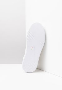 Weiße Sneaker-Sohle mit strukturierten Mustern, die ein Diamant-Griffdesign aufweist. Enthält ein Logo und eine Größenmarkierung in Rot und Grün.