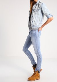 Jeansjacka i ljusblått, randig skjorta under, kombinerad med slitna ljusblå jeans och beige snörstövlar med svarta detaljer.