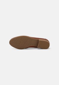 Semelle de chaussure habillée en cuir marron avec talon texturé et surface antidérapante ornée du nom de la marque "Tamaris" répété.
