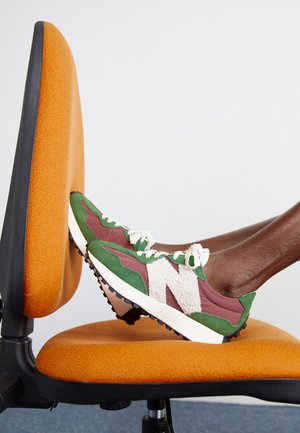 Person trägt grüne und bordeauxfarbene Sneaker und legt die Füße auf den orangefarbenen Stoffsitz und die Rückenlehne eines Bürostuhls.