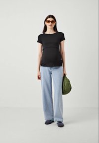 Črna kratka majica s prilagojeno silhueto, v kombinaciji s svetlo modrimi hlačami visokega pasu in z zeleno prešito torbico.