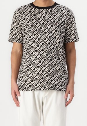T-shirt a maniche corte bianco e nero con un design geometrico, dotata di un colletto nero e un piccolo logo sul petto.