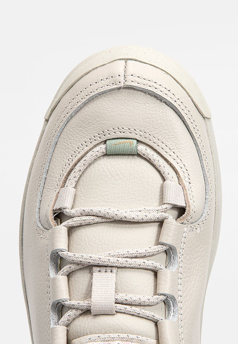 Zapatilla de cuero beige claro con puntera redondeada, superficie texturada, cordones planos en un color contrastante y un pequeño acento en la zona de los cordones.