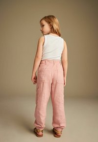 Rosa linne cargo byxor med två sid- och bakfickor, ihop med en vit ärmlös topp. Byxorna har elastiska muddar och en avslappnad passform.
