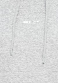Tessuto di felpa grigio chiaro con due cordini e piccolo logo bianco "JJXX STUDIO" centrato sull'area del petto.