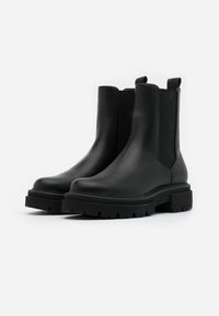 Mustat nahka nilkkurit, joissa on joustavat sivupaneelit, pyöreä kärki ja paksu kumipohja, jossa on syvät urat pidon parantamiseksi.