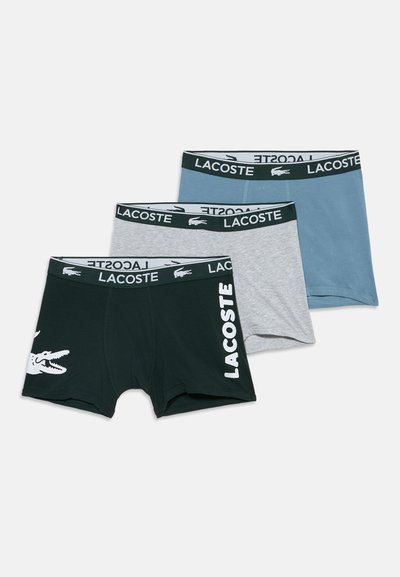Trois paires de caleçons boxer Lacoste en noir, gris et bleu avec des ceintures brandées et des détails du logo à l'avant et sur la ceinture.