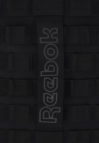 Fekete Reebok pánt, amely texturált hevederből készült, látható vízszintes sávokkal és egy jól látható sötétszürke logóval.