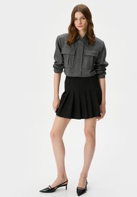 Grau croppte Jacke mit zwei Brusttaschen, kombiniert mit einem schwarzen plissierten Minikleid und schwarzen Slingback Heels mit spitzem Zehenbereich.