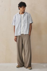 Short-sleeve, striped blue and white button-up shirt with a front pocket, paired with loose beige trousers and tan shoes.