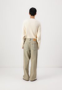 Suéter crema acanalado con hombros caídos, combinado con jeans de pierna amplia en color beige claro que tienen bolsillos traseros y una etiqueta de parche de cuero.