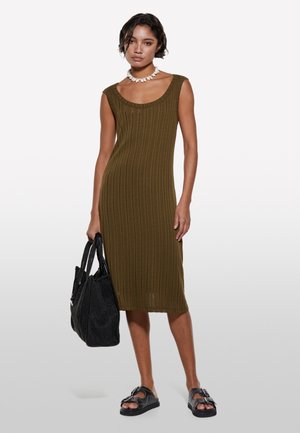 Olivgrünes ribbed Strickkleid mit Rundhalsausschnitt, seitlichem Schlitz und figurbetonter Silhouette, kombiniert mit einer schwarzen strukturierten Tragetasche und Sandalen.