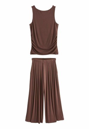 Débardeur marron côtelé sans manches associé à un pantalon marron plissé, taille haute, jambes larges sur fond blanc.