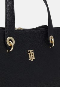 Borsa a tracolla in pelle nera texture con accenti in hardware dorato, dotata di chiusura con zip e un evidente dettaglio del logo oro sulla parte frontale.