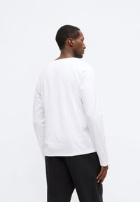 Λευκό μακρυμάνικο μπλουζάκι με χαλαρή εφαρμογή, με στρογγυλή λαιμόκοψη και ομαλή υφή, σε συνδυασμό με μαύρο παντελόνι.