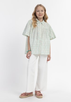Lichtgroene blouse met korte mouwen, een bloemdessin, knoopsluiting aan de voorkant en geplooide details, gecombineerd met witte wijde broekspijpen en roze espadrilles.
