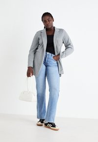 Blazer cinza estruturado com lapelas em bico, combinado com uma blusa preta, jeans azul claro e sapatilhas atléticas pretas. Os acessórios incluem uma bolsa branca.