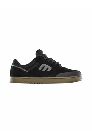 Zapatilla negra de corte bajo con logo gris en el lateral, cordones negros y suela beige, mostrada de perfil sobre fondo blanco.