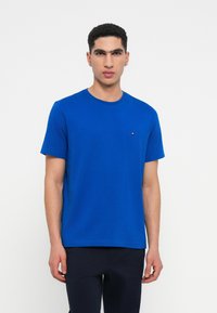 Zila kokvilnas T-kreklu ar apaļu kakla izgriezumu, īsām piedurknēm un nelielu logotipa akcentu uz krūšu daļas. Gluda tekstūra un parasta piegrieztne.